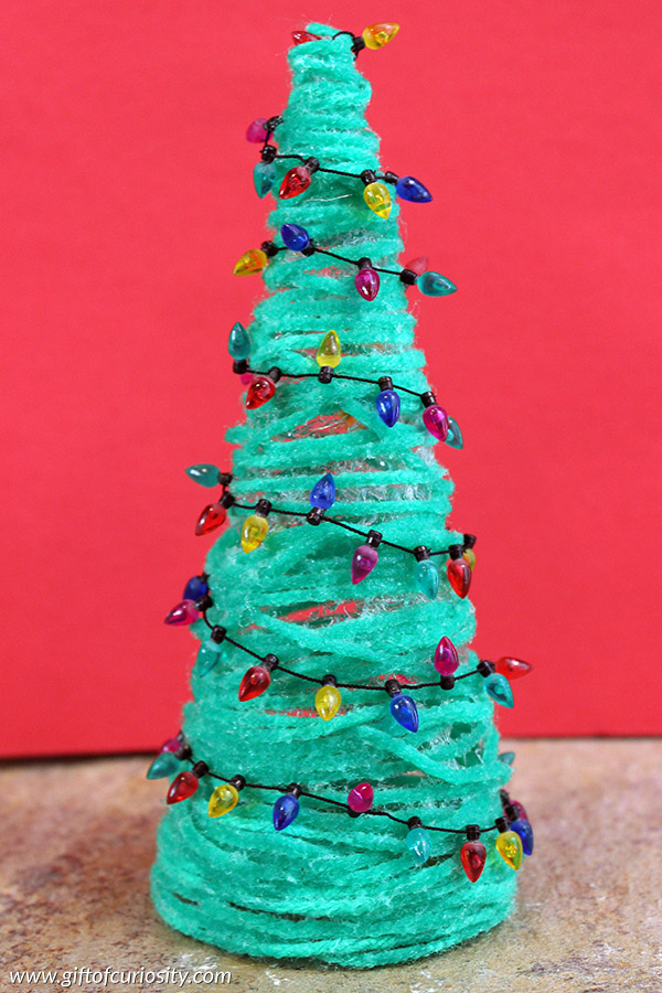 Build this cute Christmas tree craft for the holidays using green yarn and Mod Podge. Then trip your tree with mini lights, jeweled stickers, and more! || Gift of Curiosity